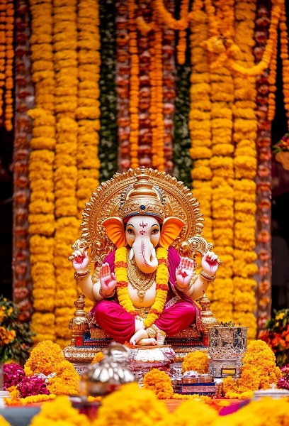 Lord Ganesha idol decorated with flowers and modaks, surrounded by devotees during Ganesh Chaturthi festival celebrations.